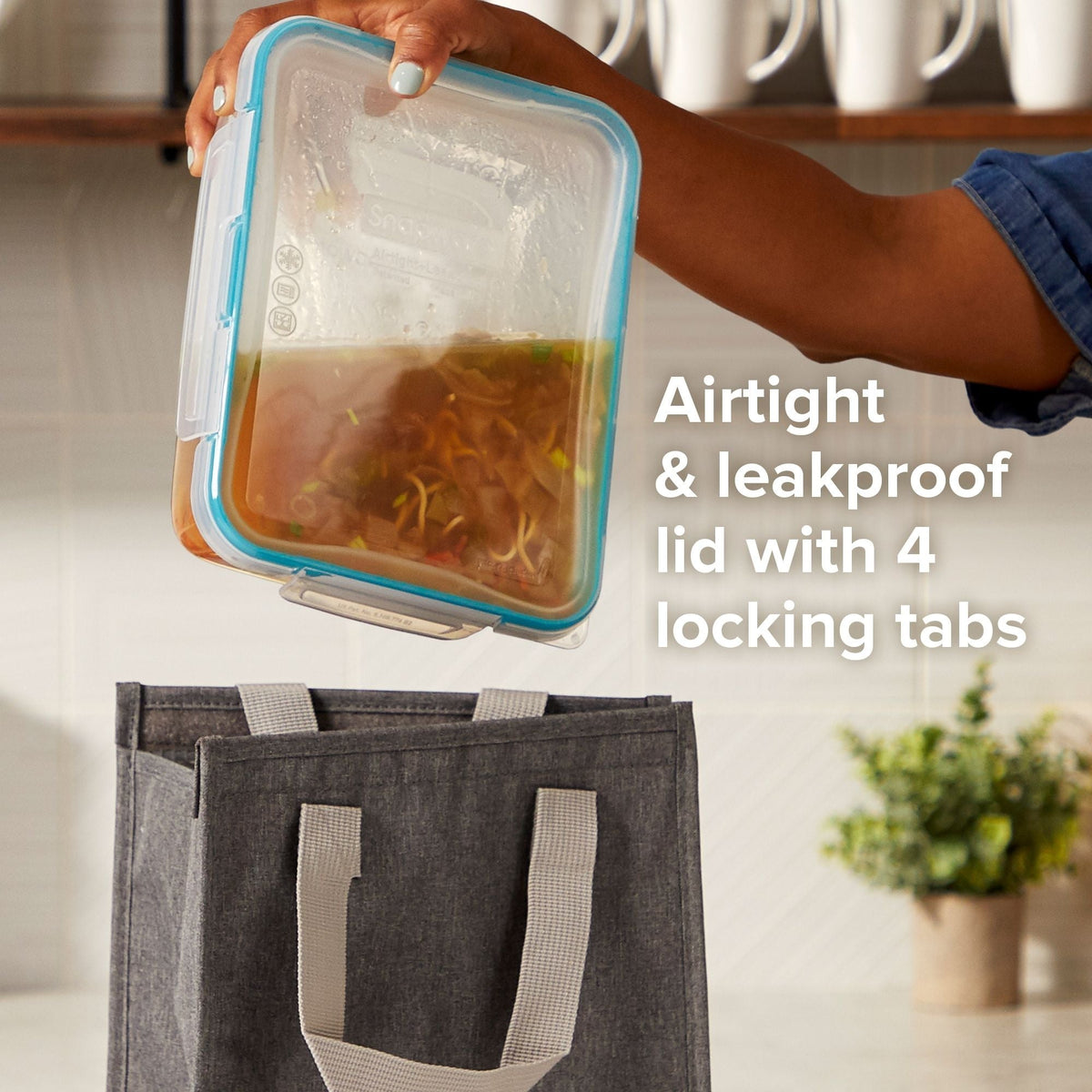 Person holding a BPA-free food container with airtight lid, next to a gray tote bag.